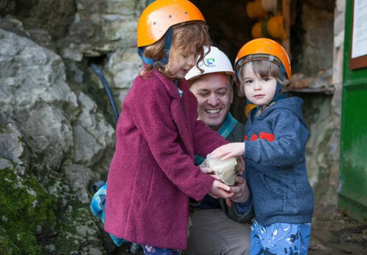 A man and 2 children, wearing mining helmets and smiling.
